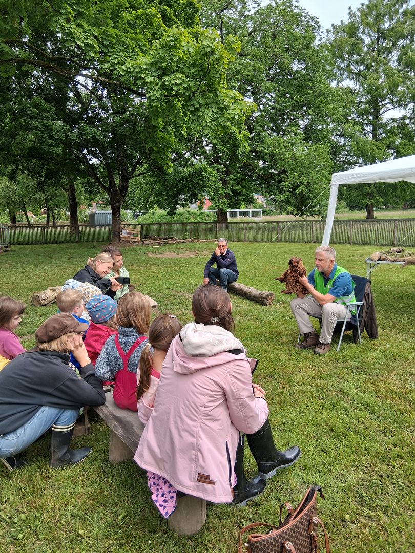 Biberklassenzimmer, Kinder sitzen im Halbkreis auf einer Wiese und lassen sich ein Biber-Stofftier erklären.